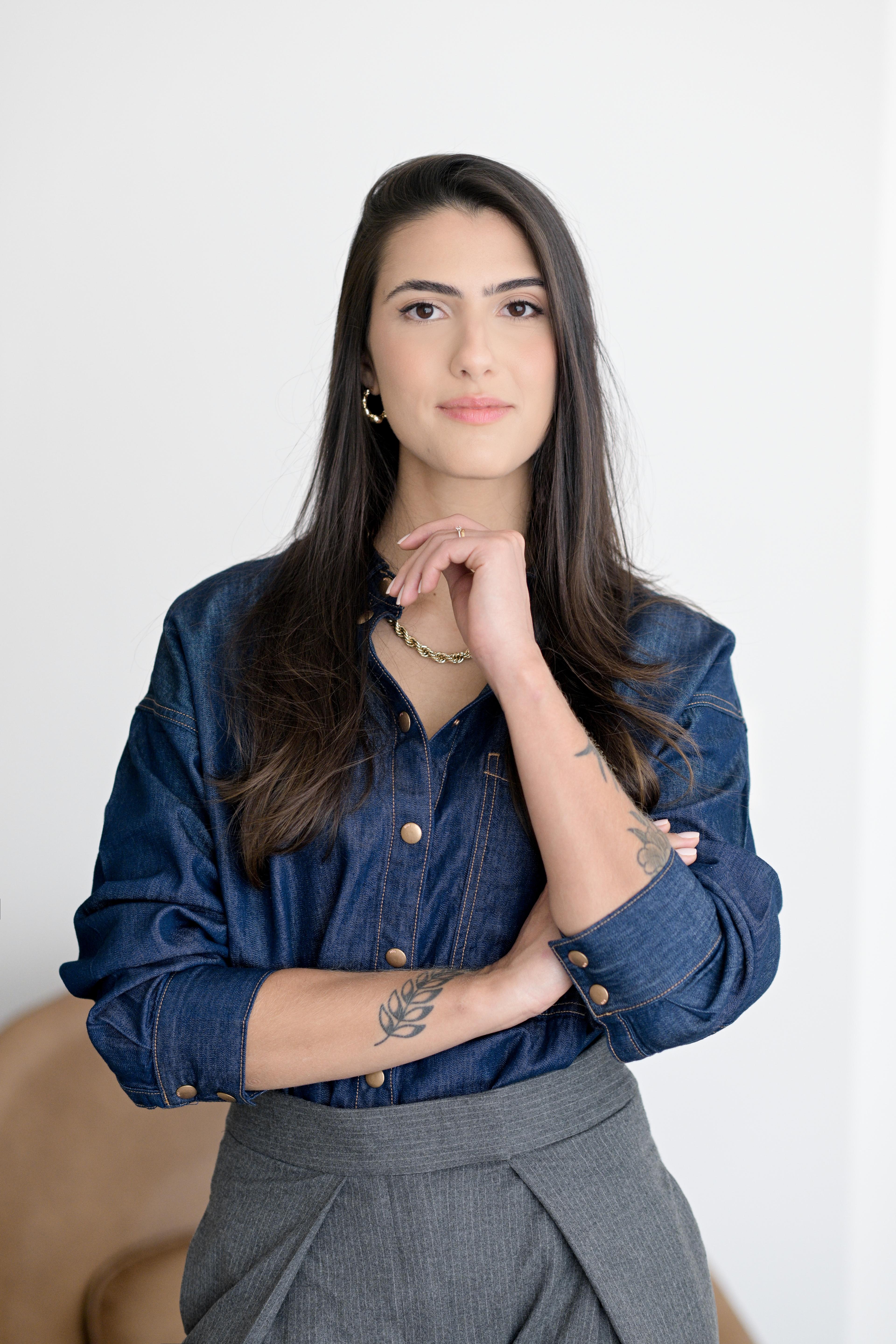 Júlia Martins em retrato profissional, com camisa jeans e sorriso acolhedor